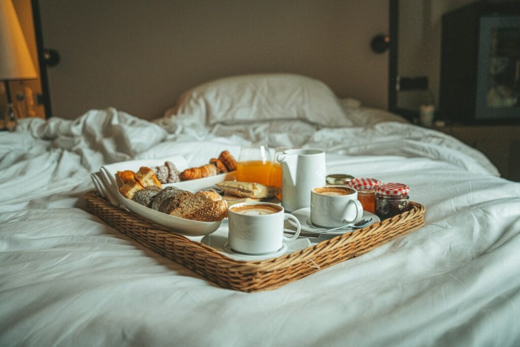 Wicker tray of pastries, coffee and juice set on the white sheets of a hotel bed