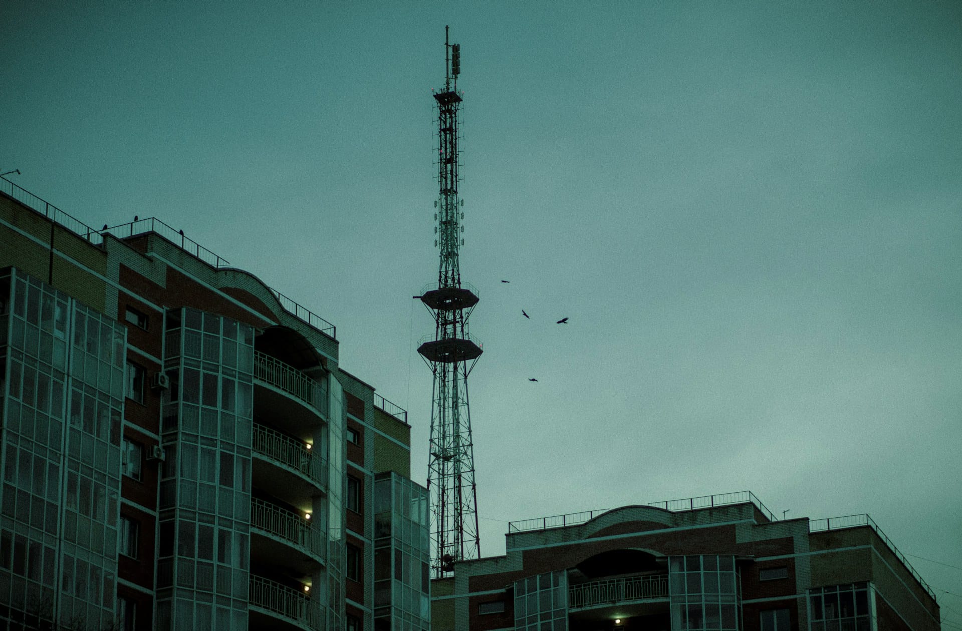 Lattice broadcast mast standing between two buildings at dusk