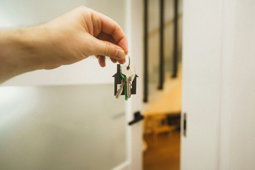 Une main tendant un trousseau de clés à porte-clé en forme de maison, devant une porte ouverte