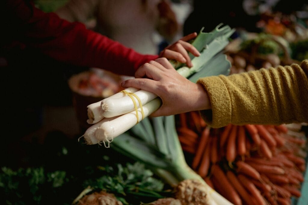 Une main saisissant une botte de poireaux au-dessus d’un étal de légumes frais