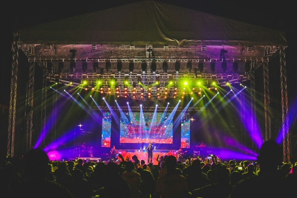 Concert stage lit by a rig of spotlights, audience in silhouette in the foreground