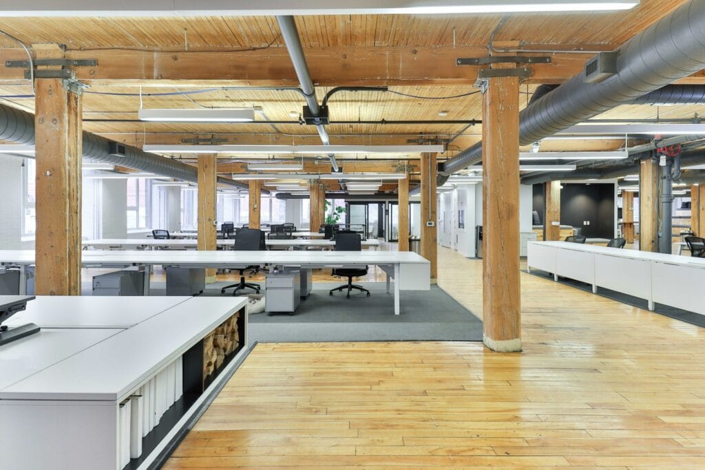 Plateau de bureaux ouvert, poteaux et plafond en bois, rangées de postes de travail inoccupés