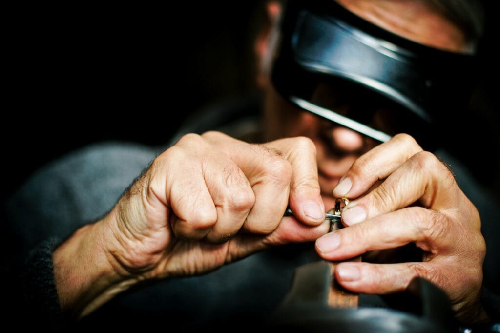 A jeweller wearing a head loupe examining a gold piece held between his fingers