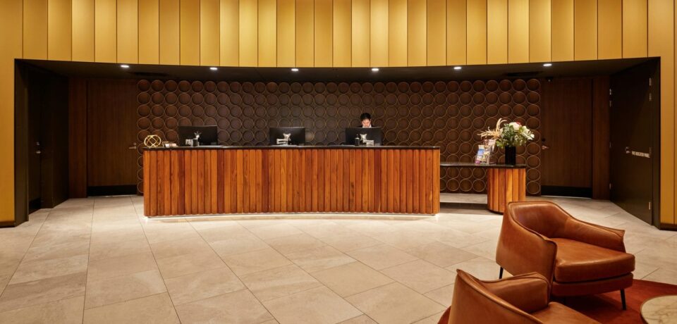 Hall de réception d’un hôtel : comptoir en bois éclairé et fauteuils en cuir au premier plan
