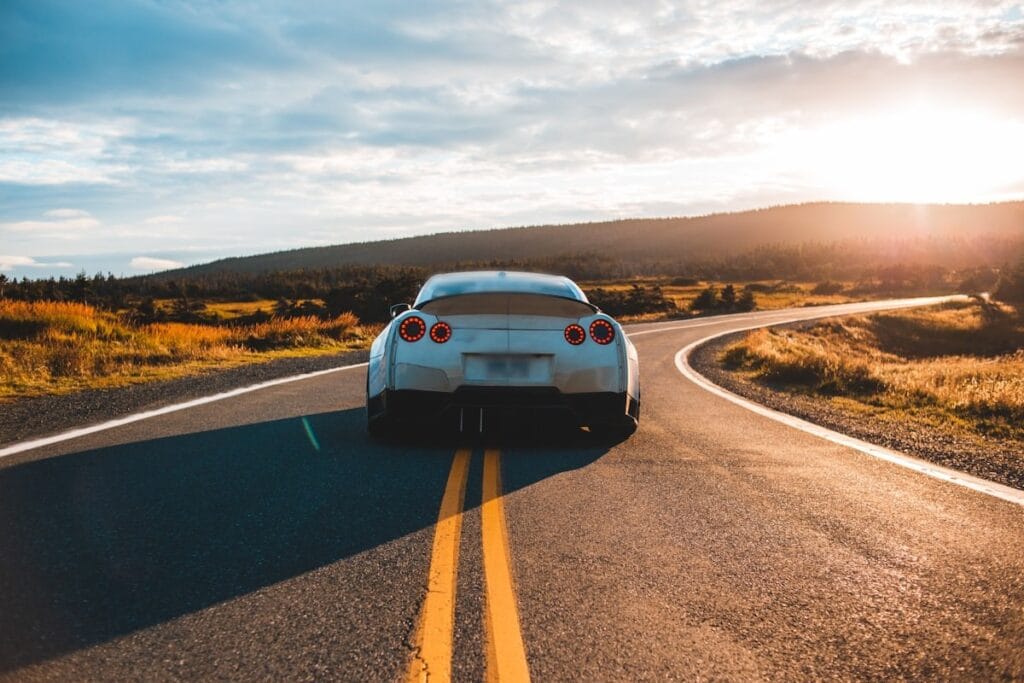 White sports car seen from behind on a country road at sunset, a double yellow line down the middle